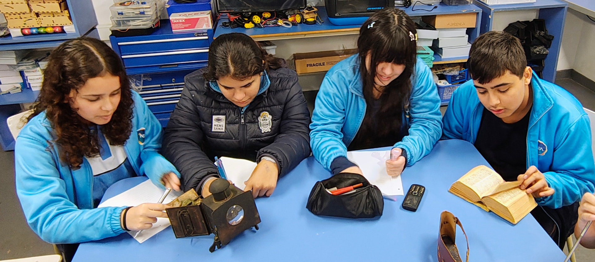 Estudiantes investigan objetos tecnológicos antiguos sobre una mesa del laboratorio